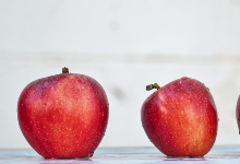 2 juicy red delious and tasty looking apples sitting atop a table screaming please eat me I'm healthy!