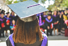 Graduate wearing black cap and gown with purple tassle