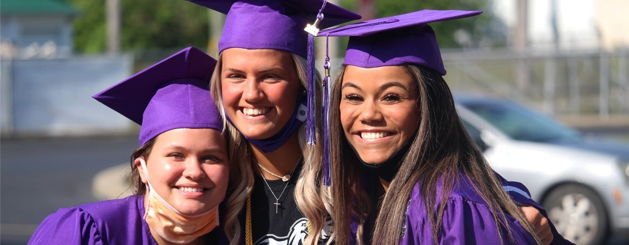 Purple Cap and Gown with three girls smiling