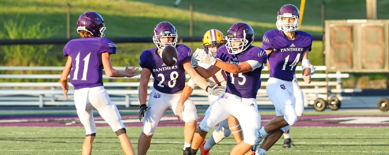 Football team wearing purple tossing football during game